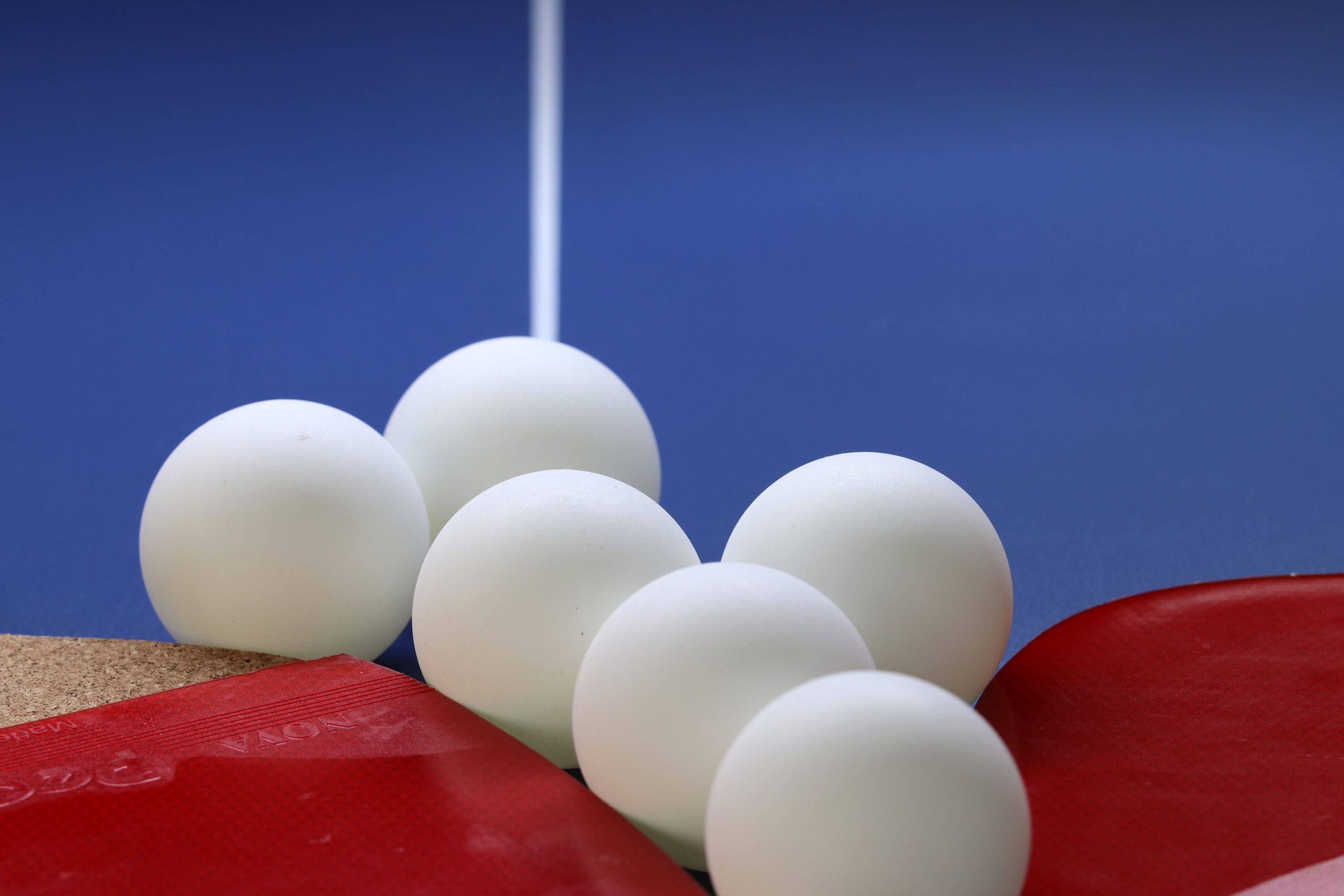 Tischtennisbälle neben Tischtennisschlägern vor dem Hintergrund eines Tischtennistischs